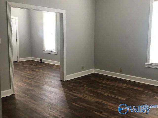 empty room featuring baseboards, plenty of natural light, and dark wood finished floors