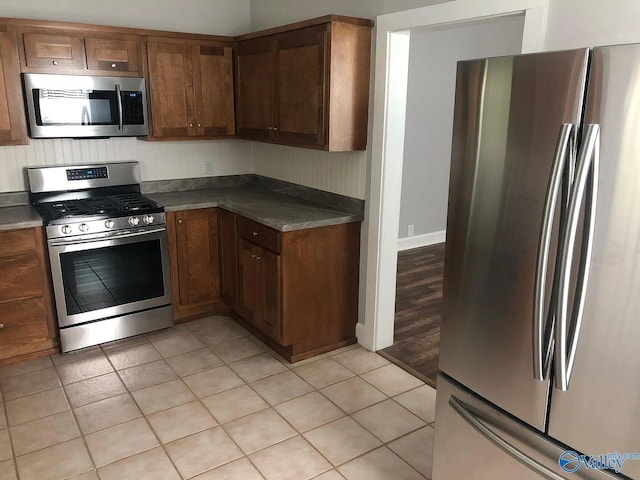 kitchen with light tile patterned floors, appliances with stainless steel finishes, and brown cabinetry