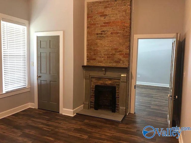unfurnished living room featuring baseboards, dark wood finished floors, and a wealth of natural light