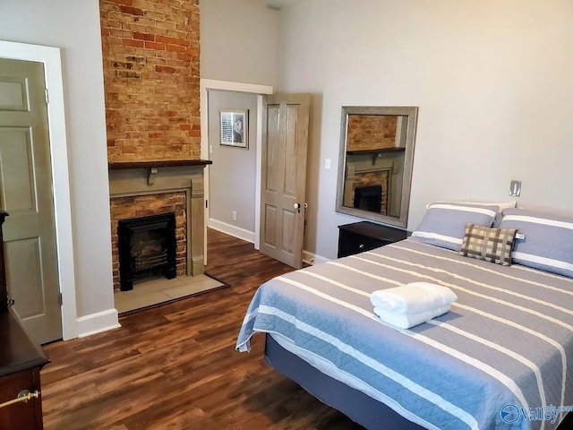 bedroom featuring baseboards, a fireplace, wood finished floors, and a towering ceiling