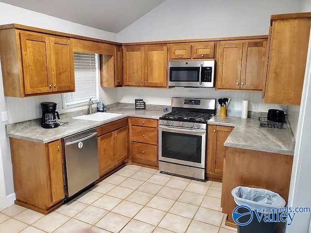 kitchen with brown cabinetry, lofted ceiling, light countertops, a sink, and stainless steel appliances