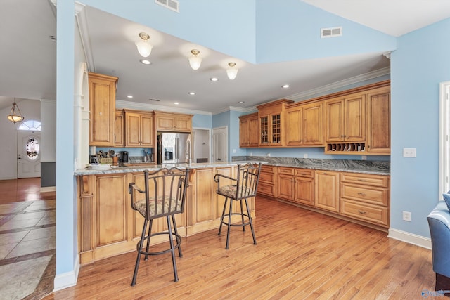 kitchen featuring kitchen peninsula, stainless steel fridge, ornamental molding, light hardwood / wood-style flooring, and a breakfast bar area