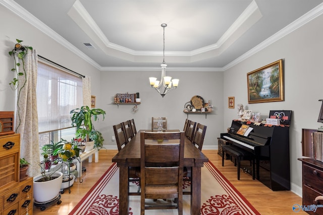 dining room featuring a chandelier, light wood finished floors, a raised ceiling, ornamental molding, and visible vents
