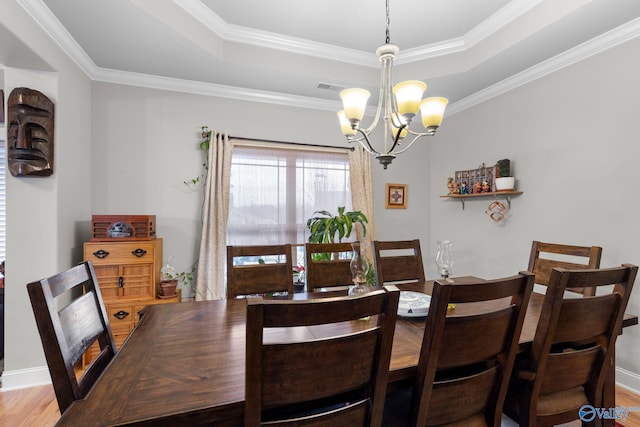dining room with a tray ceiling, wood finished floors, ornamental molding, and a notable chandelier