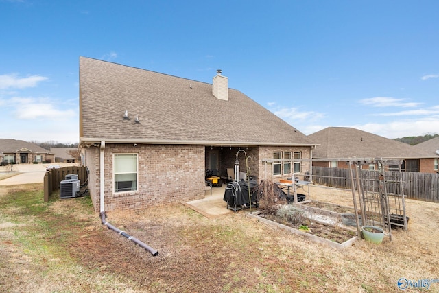 rear view of house with a garden, cooling unit, fence, brick siding, and a shingled roof