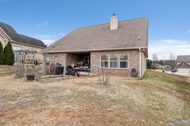 rear view of house with roof with shingles, a garden, a chimney, brick siding, and a yard