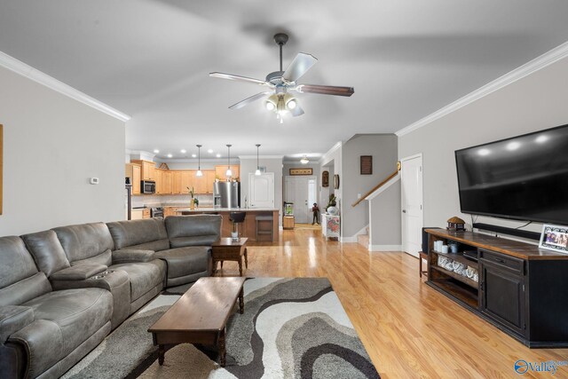 living room with ornamental molding, baseboards, light wood-style flooring, stairs, and ceiling fan