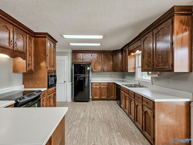 kitchen featuring light wood-type flooring, black appliances, a textured ceiling, and sink