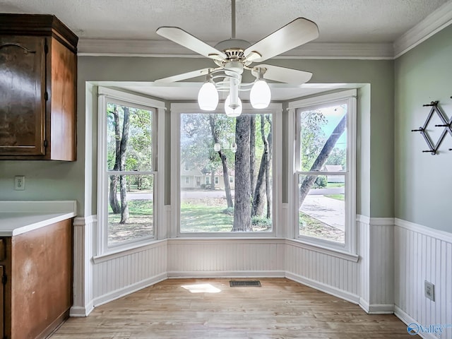 unfurnished dining area featuring light hardwood / wood-style flooring, a textured ceiling, ceiling fan, and crown molding