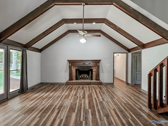 unfurnished living room with lofted ceiling with beams, wood-type flooring, ceiling fan, and a brick fireplace