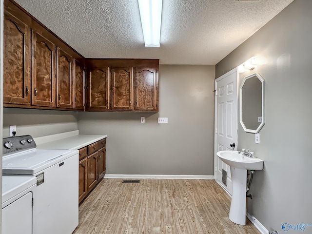 washroom featuring light wood-type flooring, a textured ceiling, washing machine and clothes dryer, and cabinets