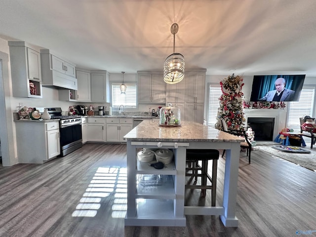 kitchen featuring appliances with stainless steel finishes, dark hardwood / wood-style flooring, light stone counters, sink, and decorative light fixtures