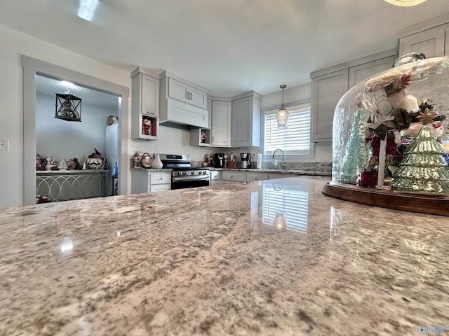 kitchen with light stone countertops, sink, stainless steel stove, and decorative light fixtures