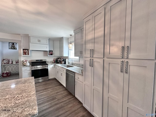 kitchen with pendant lighting, dark wood-type flooring, sink, light stone counters, and stainless steel appliances