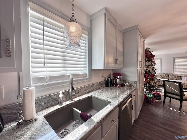 kitchen with light stone counters, stainless steel dishwasher, dark wood-type flooring, sink, and hanging light fixtures