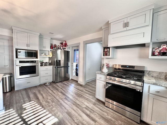 kitchen featuring white cabinetry, stainless steel appliances, light stone counters, light wood-type flooring, and custom exhaust hood