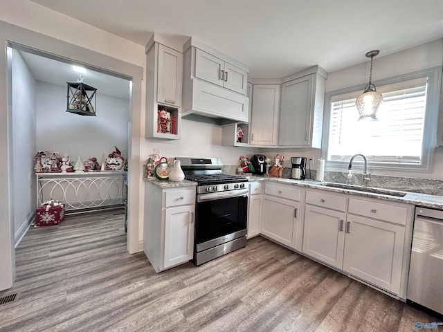 kitchen with pendant lighting, sink, light hardwood / wood-style flooring, light stone countertops, and appliances with stainless steel finishes