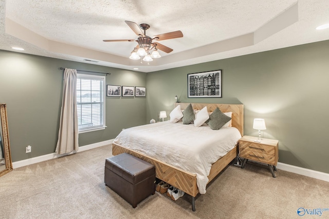 bedroom with a textured ceiling, visible vents, light colored carpet, and a tray ceiling