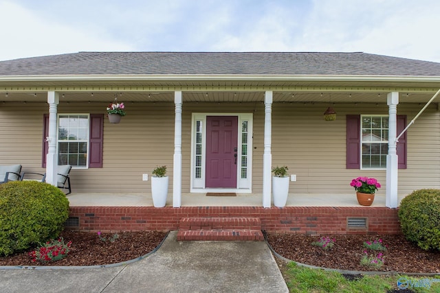 view of exterior entry with covered porch, a shingled roof, and crawl space
