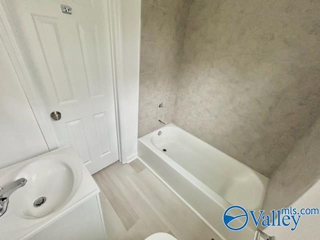 bathroom with hardwood / wood-style flooring, shower / bathing tub combination, sink, and tile walls