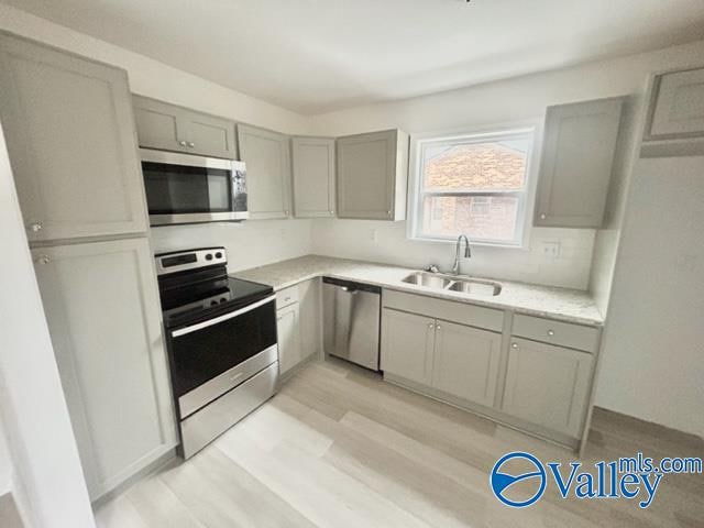 kitchen featuring gray cabinetry, stainless steel appliances, light hardwood / wood-style floors, and sink