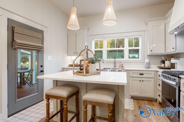 kitchen featuring custom range hood, stainless steel range with gas stovetop, a kitchen breakfast bar, light countertops, and a sink