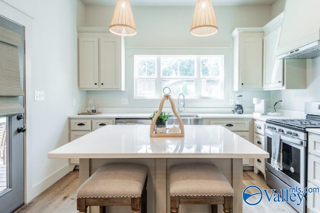 kitchen with stainless steel range with gas cooktop, custom range hood, light wood finished floors, and a kitchen bar