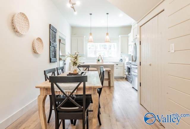 dining area with light wood-style floors, baseboards, and rail lighting