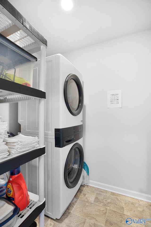 washroom featuring laundry area, baseboards, stone finish floor, and stacked washer / drying machine