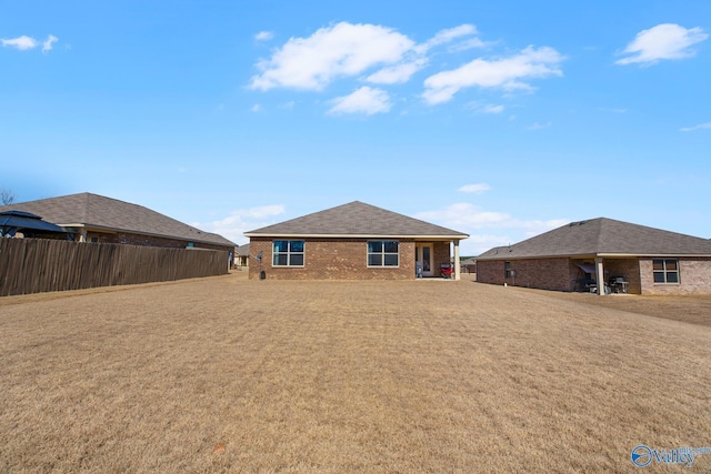 back of house with a yard, brick siding, fence, and roof with shingles