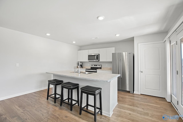 kitchen with stainless steel appliances, light wood finished floors, a sink, and a kitchen breakfast bar