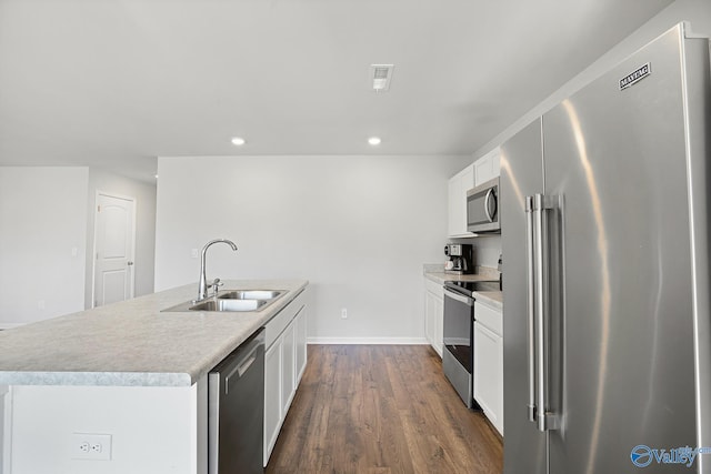 kitchen featuring dark wood finished floors, stainless steel appliances, white cabinetry, a sink, and an island with sink