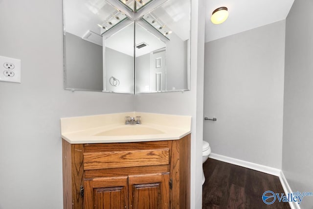 half bath with vanity, visible vents, toilet, wood finished floors, and baseboards