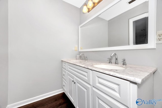 bathroom with a sink, baseboards, double vanity, and wood finished floors