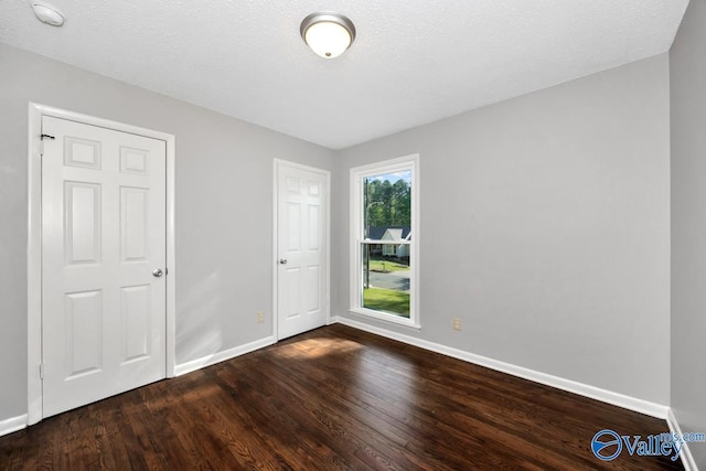 spare room featuring a textured ceiling, baseboards, and dark wood finished floors