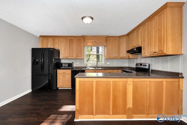 kitchen featuring a sink, dark countertops, a peninsula, under cabinet range hood, and stainless steel appliances