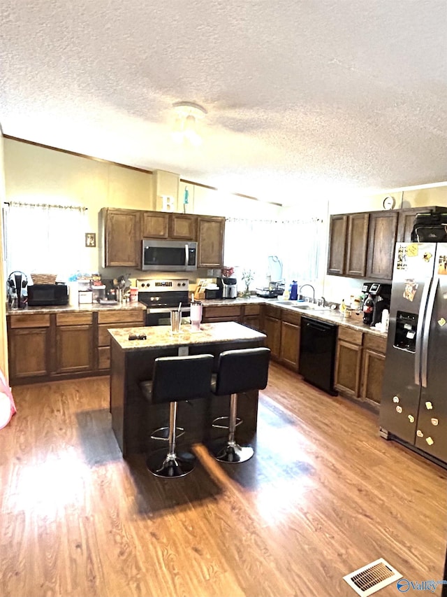 kitchen featuring visible vents, a center island with sink, appliances with stainless steel finishes, light wood-style floors, and a textured ceiling