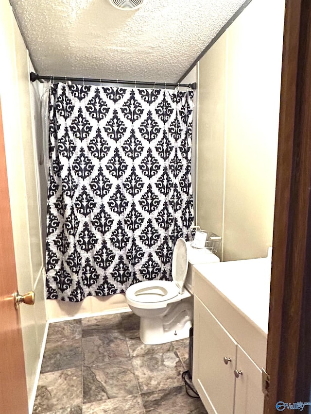 bathroom featuring toilet, stone finish floor, a textured ceiling, a shower with shower curtain, and vanity