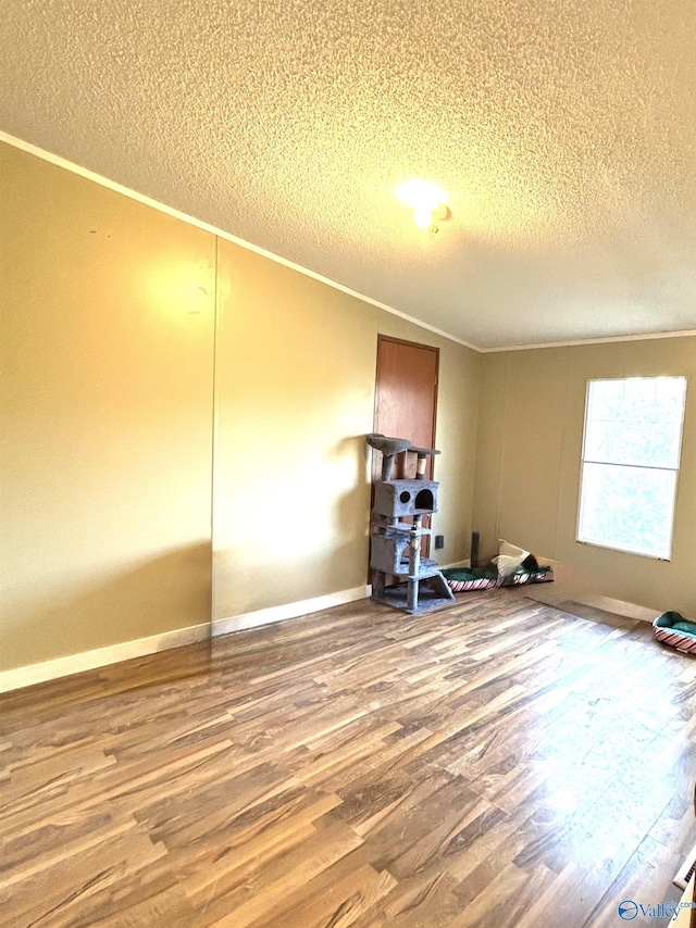 empty room with baseboards, a textured ceiling, wood finished floors, and crown molding