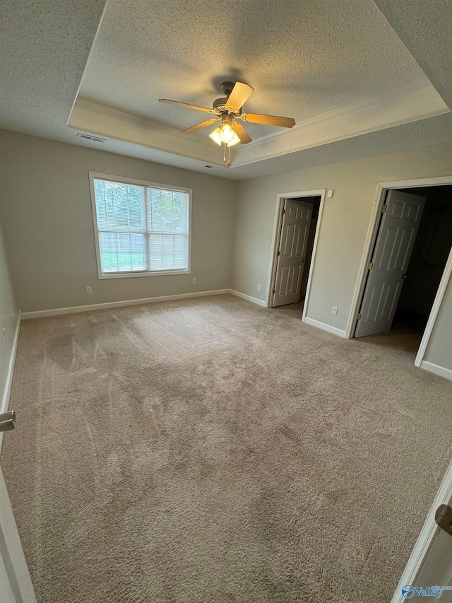 unfurnished bedroom featuring ceiling fan, light colored carpet, a textured ceiling, and a tray ceiling