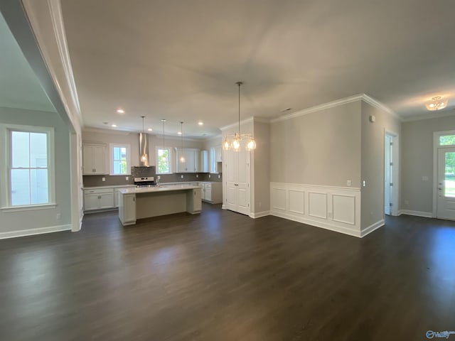 kitchen featuring a kitchen island, white cabinets, hanging light fixtures, dark wood-type flooring, and wall chimney range hood