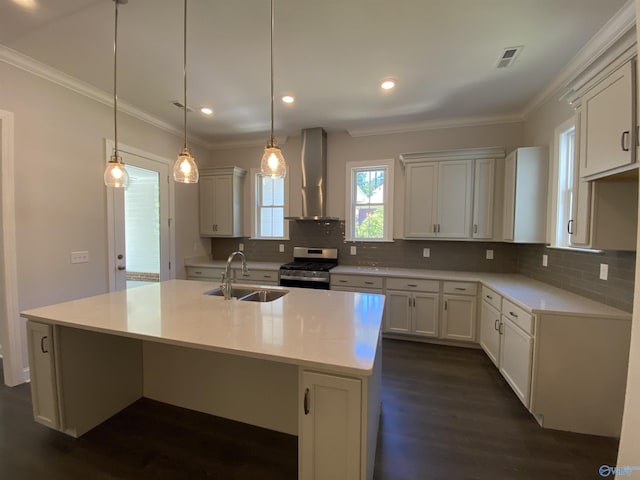 kitchen featuring wall chimney range hood, sink, a kitchen island with sink, stainless steel range with gas stovetop, and decorative light fixtures