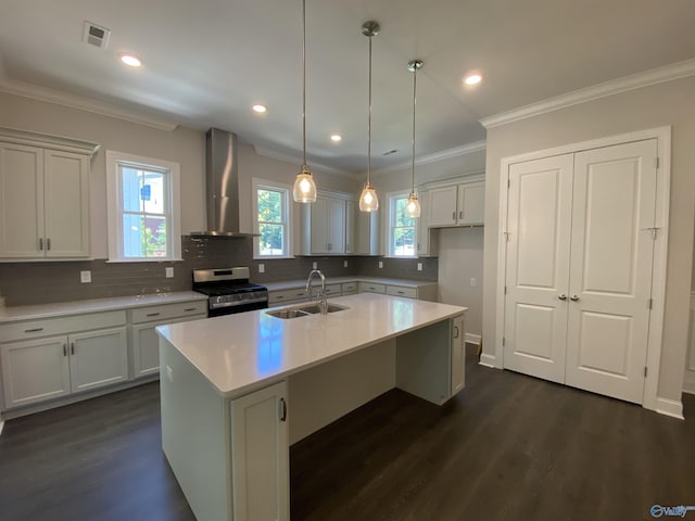 kitchen with sink, stainless steel gas stove, a center island with sink, decorative light fixtures, and wall chimney exhaust hood