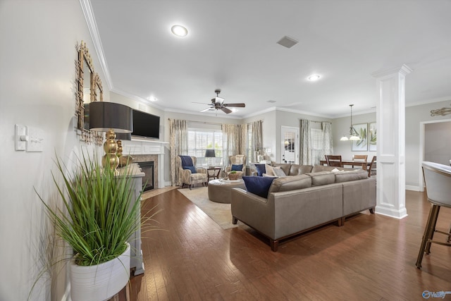 living room with visible vents, a fireplace with flush hearth, hardwood / wood-style flooring, crown molding, and decorative columns