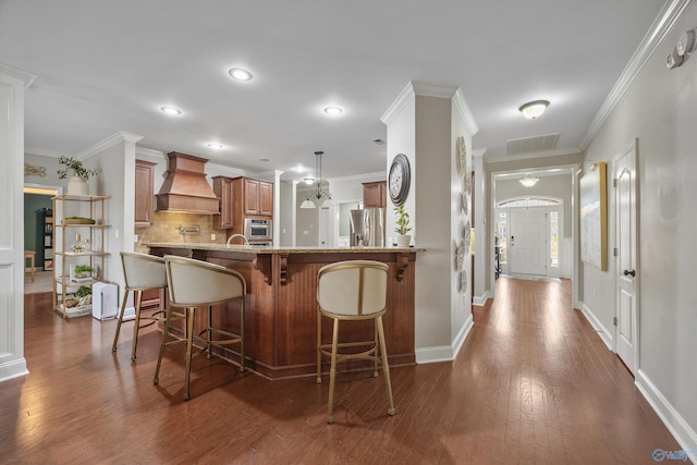 kitchen with a breakfast bar, stainless steel refrigerator with ice dispenser, premium range hood, and ornamental molding