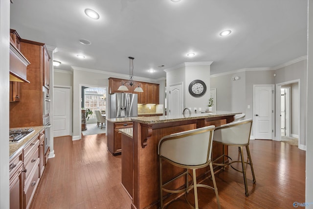 kitchen featuring brown cabinets, appliances with stainless steel finishes, a breakfast bar, and an island with sink