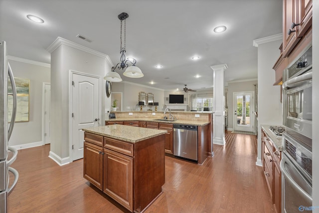 kitchen featuring brown cabinetry, decorative columns, a sink, stainless steel appliances, and a center island