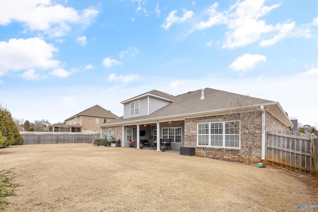 back of house featuring roof with shingles, a yard, a fenced backyard, a patio area, and brick siding