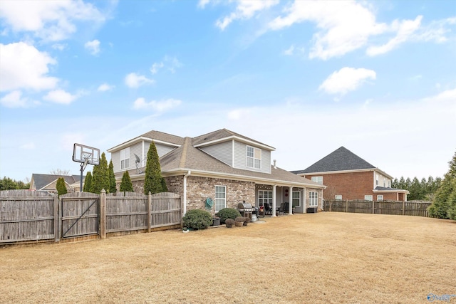 rear view of house with brick siding, roof with shingles, a lawn, a fenced backyard, and a patio area