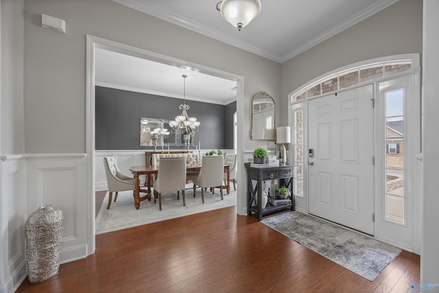 foyer featuring a wainscoted wall, dark wood finished floors, ornamental molding, a decorative wall, and a notable chandelier